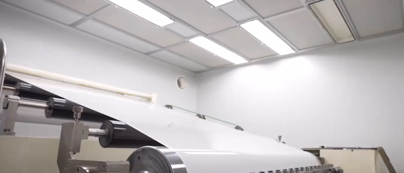 Inside the GSUIT factory: film running over the rollers of a coating line under bright ceiling lights.