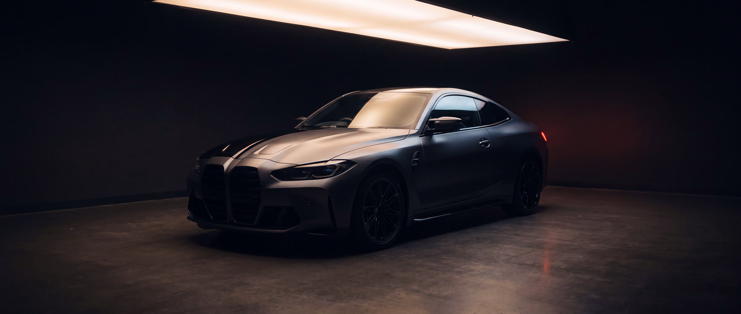 A dark performance coupe in a black studio, a crisp diagonal film edge dividing gloss paint from satin across its bonnet.